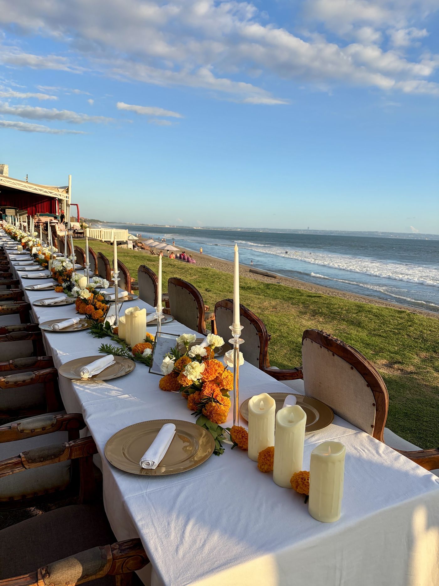 A long table laid with candles and marigolds, the ocean behind it