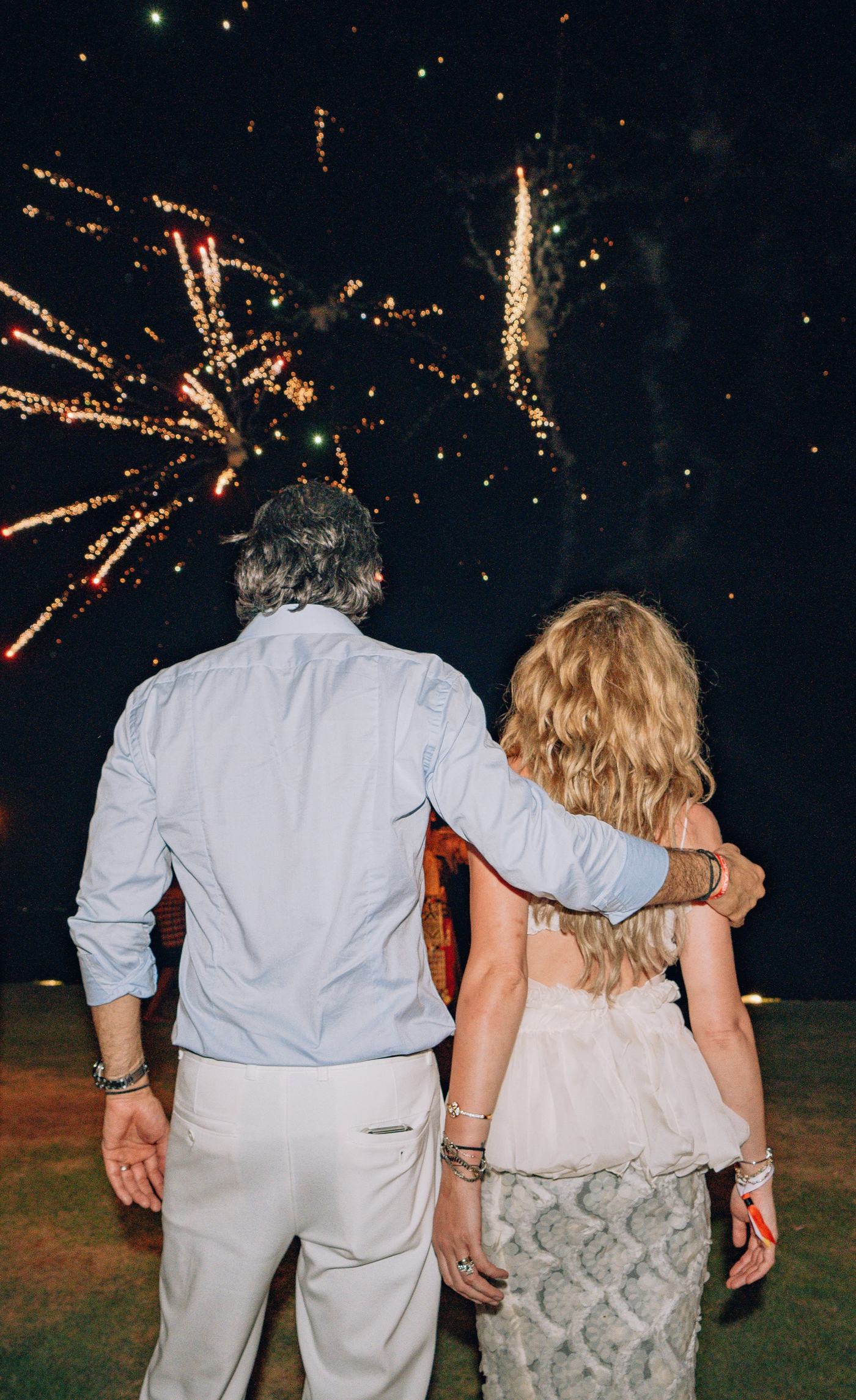 Two guests seen from behind watching fireworks burst over the darkness