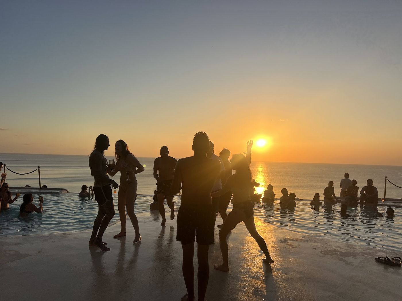 Guests silhouetted at an infinity pool as the sun drops to the horizon